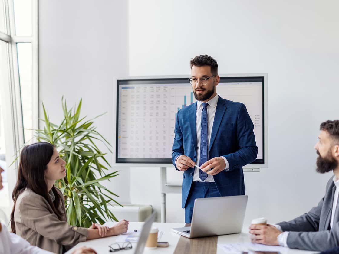 Portrait of young team leader standing at conference table presenting information to company decision makers. 