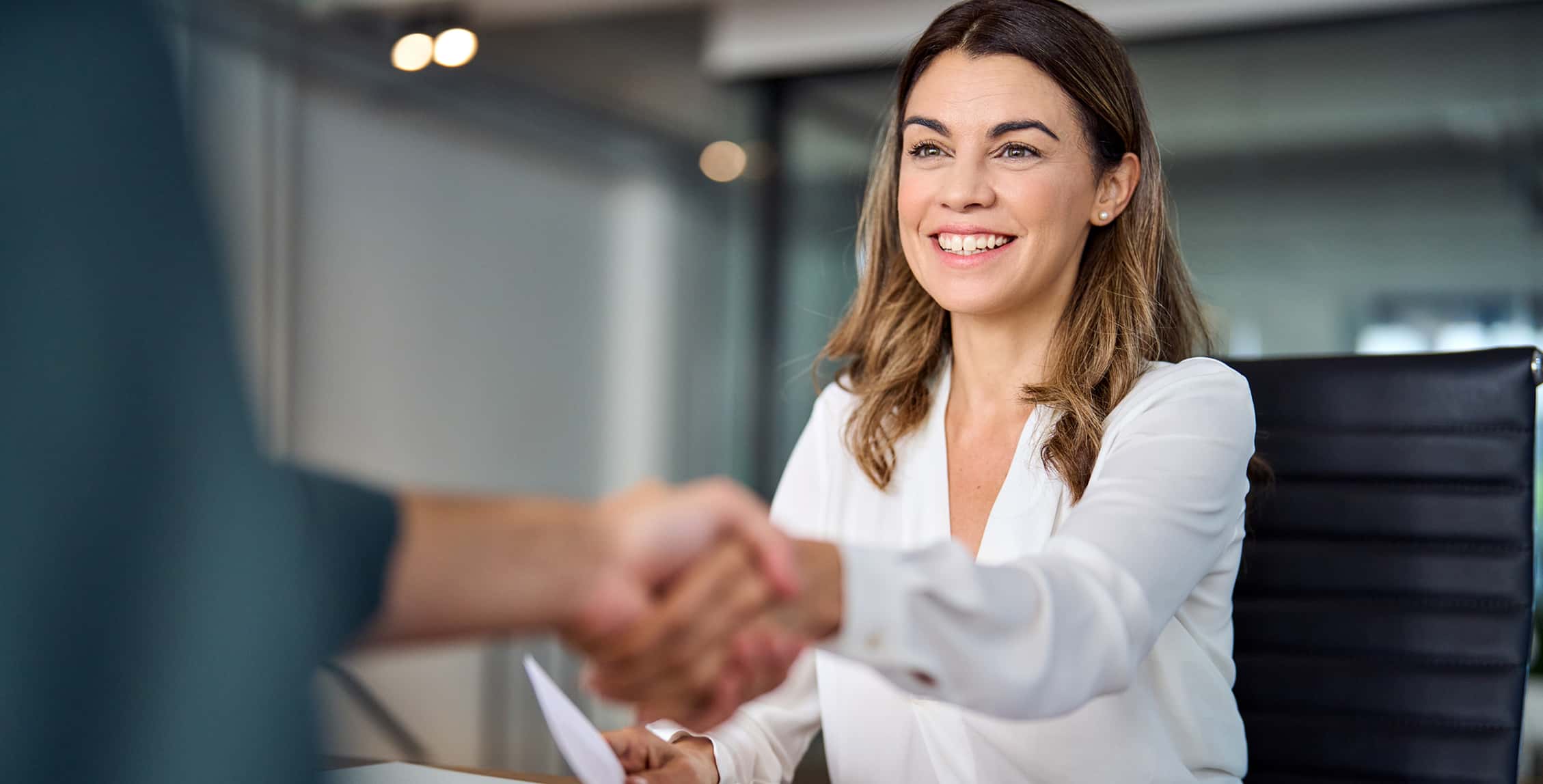 Smiling business woman shaking hand across a conference room table